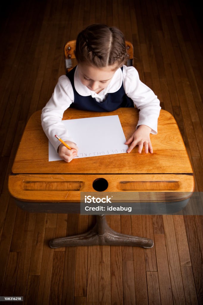 Chica joven estudiante escribir mientras se distiende en la escuela escritorio - Foto de stock de 6-7 años libre de derechos