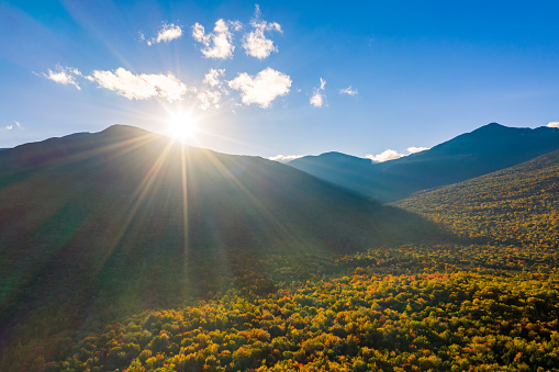 Aerial shot with sun rays flaring at sunset from behind Mount Washington, New Hampshire, on a late autumn afternoon.