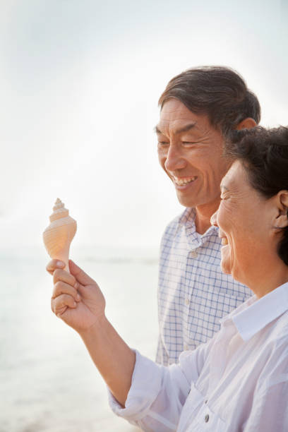 istock Older Chinese couple examining shell on beach 1083164956
