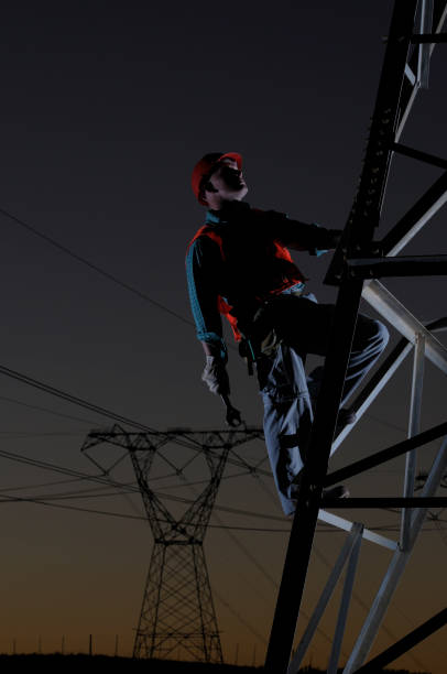 Silhouette electrical engineer working at the site of electricity pylon with orange sky