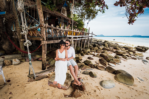 Loving couple on a rope swing on the shore of a sea. Man and woman resting on the Islands in Asia. Guy and girl hugging on the beach. Honeymoon by the sea. Newly married couple. Lovers on the sea.