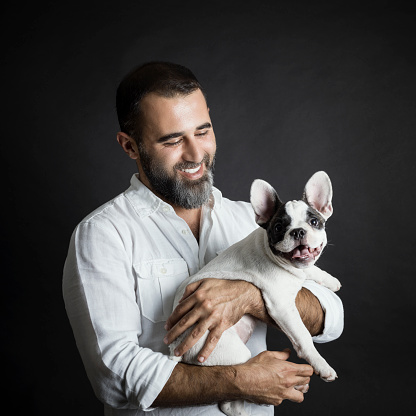 Man with his dog on black background, studio shot. French bulldog puppy