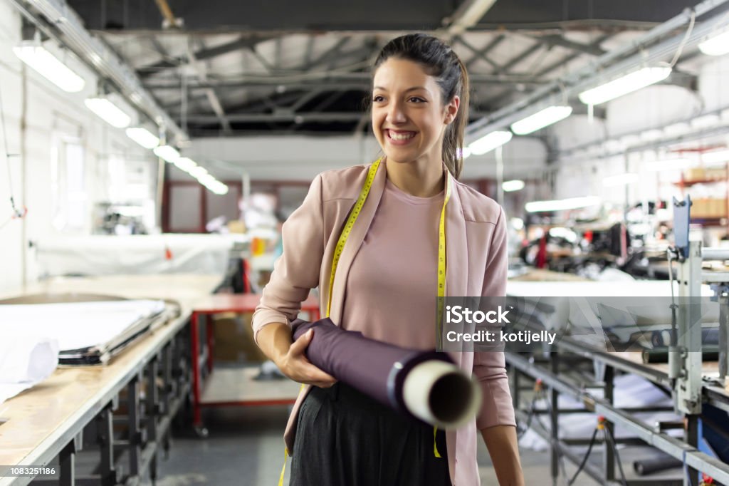 Smiling young woman in a fashion factory Smiling young woman working in a fashion factory Occupation Stock Photo