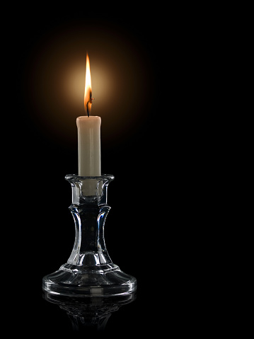 Burning candle in a glass candlestick it is isolated on the black