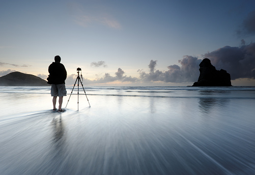 A photographer standing in the surf on a beach in New Zealand