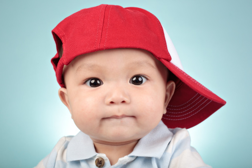 A closeup shot of a cute happy little boy in a hat sitting on a grass