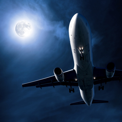 jet airplane landing at night in close-up with full moon and wispy clouds, square frame