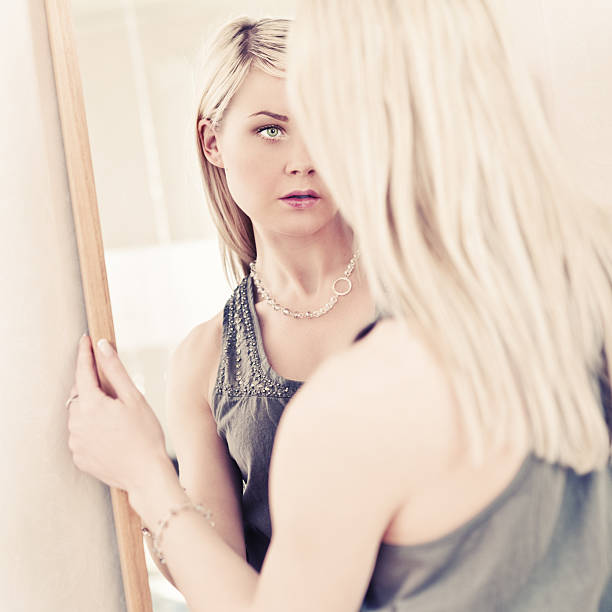 Sad blonde woman stands against a stone wall, lost in thought, reflecting loneliness and distress. Her expression conveys sadness, worry, and contemplation, evoking grief and melancholy