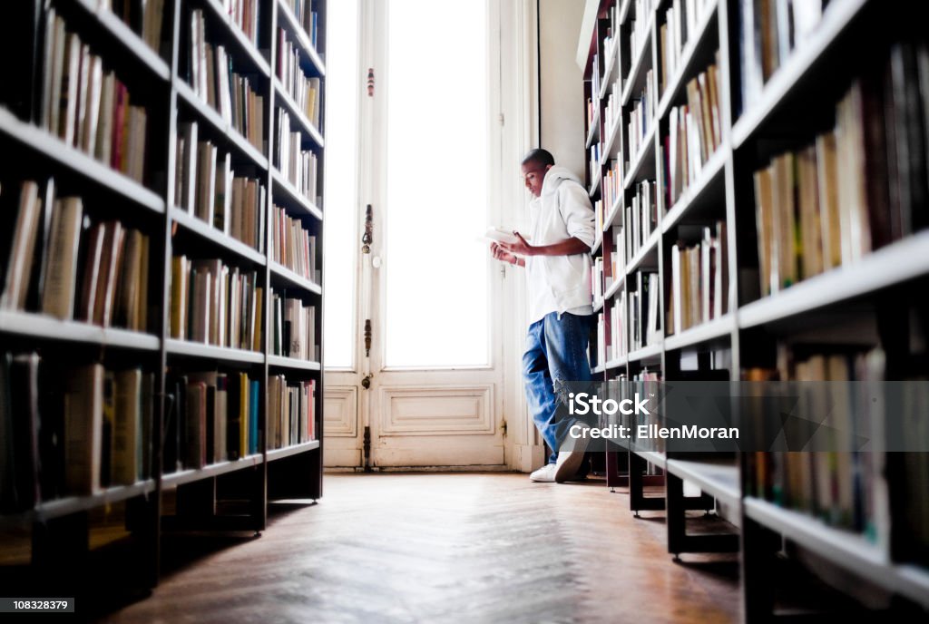 Jovem lendo em uma biblioteca - Foto de stock de Biblioteca royalty-free