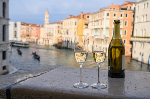 Bottle of red wine with two glasses on marble railing of Rialto Bridge in Venice, Italy. Shallow DOF with selective focus on the foreground.