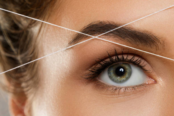 Eyebrow threading - epilation procedure for brow shape correction Close-up of female eye with a thread. Eyebrow threading - epilation procedure for brow shape correction eyebrow stock pictures, royalty-free photos & images