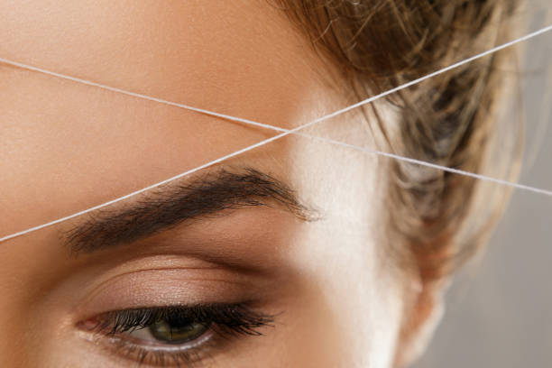 Eyebrow threading - epilation procedure for brow shape correction Close-up of female eye with a thread. Eyebrow threading - epilation procedure for brow shape correction hair threading stock pictures, royalty-free photos & images