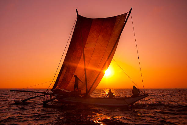 As the sun sets, the tranquil beach is bathed in soft hues of pink and purple. Boat with sail is visible on the horizon, gently drifting on the water. Boracay, Philippines.