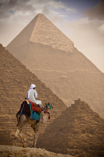 Cairo, Egypt - April 29, 2023: Portrait of a man with his camel and in the background view of the Great Pyramid in Giza