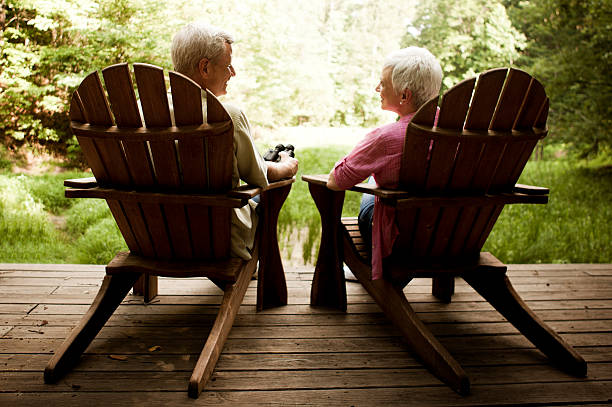coppia senior rilassarsi in adirondack sedie su un ponte di legno - adirondack chair foto e immagini stock
