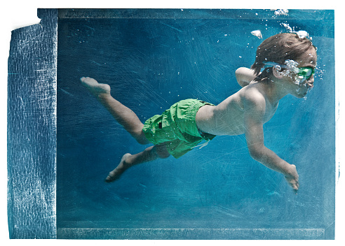 eighth years old kid swimming under the water on a pool.