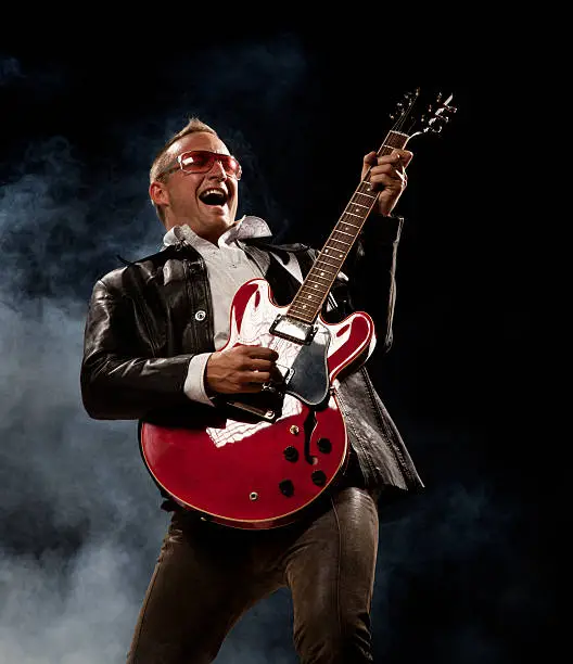 Photo of Rocker Man Plays Electric Guitar and Sings. Smoky Black Background.