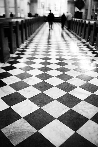 Point of view of a male adult standing looking down wearing a three quarter pants and a sneakers shoe on square cube tiles flooring in monotone.
