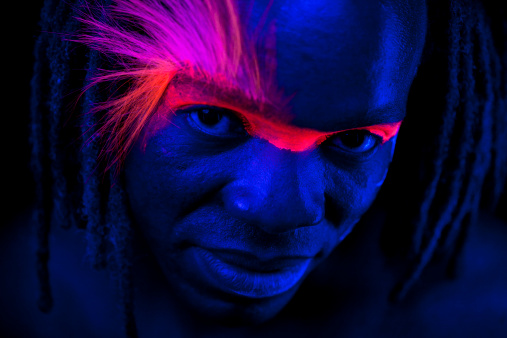 Portrait of a man under black lights with glowing hair, and makeup. No filters were used to create this effect - this is UV lighting creating the glow-in-the-dark hair, and makeup. Extremely low light situation with high ISO settings. 