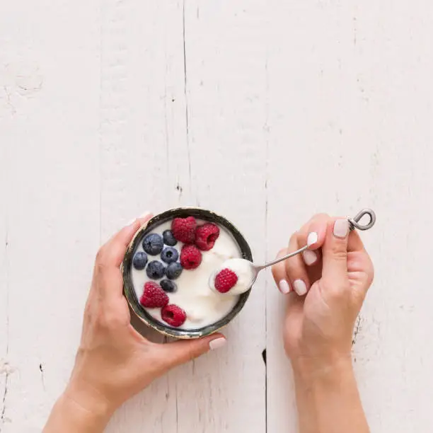 Photo of Top view on girl's hands holding a bowl with organic vanilla yogurt with fresh berries. Healthy eating.