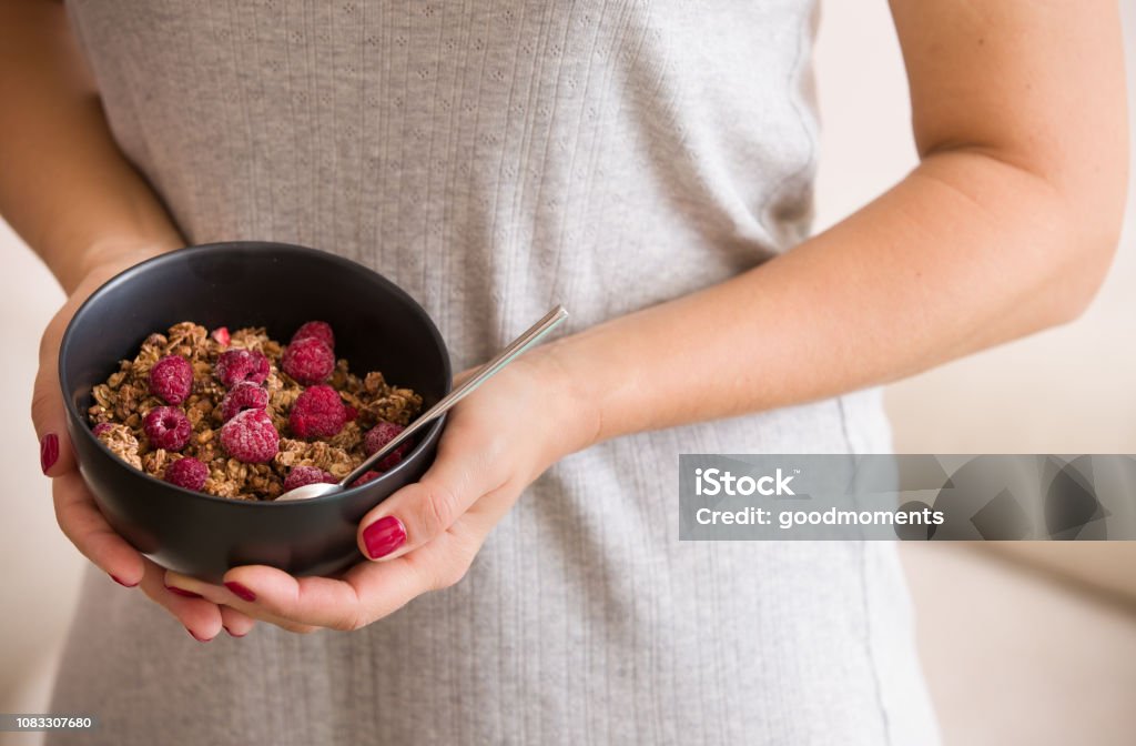 Gros plan des mains d’une jeune femme tenant un bol noir avec granola organique avec lait de coco et framboises. Mode de vie sain. - Photo de Adulte libre de droits