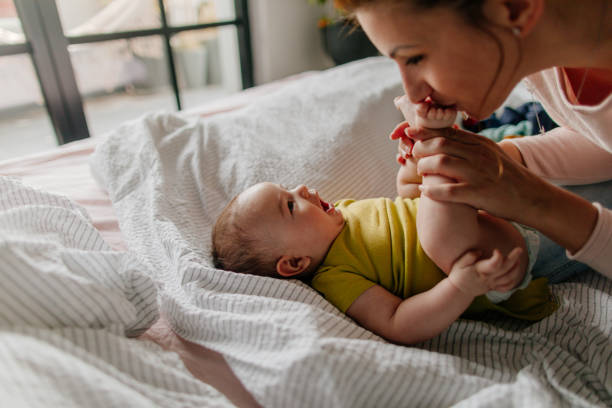 Smiling baby and his mom Portrait of a little smiling baby boy and his mom, kissing his tiny feet right after waking up in his nursery 2 5 months stock pictures, royalty-free photos & images