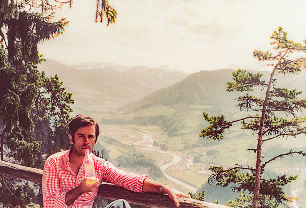 Vintage photo of a man drinking a soft drink in front of a scenic landscape in the background.