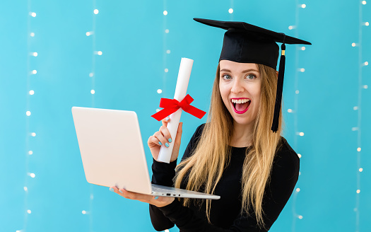 Young woman with a graduation diploma and laptop pc on a shiny light background