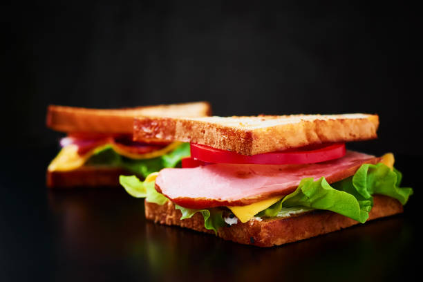 istock Homemade sandwich with lettuce and ham on a black background, close up 1083344582