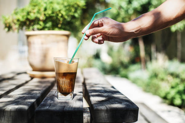 Putting a straw in a glass of ice coffee (freddo cappuccino) Putting a straw in a glass of ice coffee (freddo cappuccino) on a wooden table. Sunny day in the garden freddo cappuccino stock pictures, royalty-free photos & images