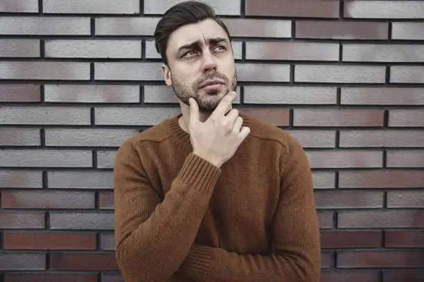 Photo of Young hipster guy wearing have some ideas on brick wall background.