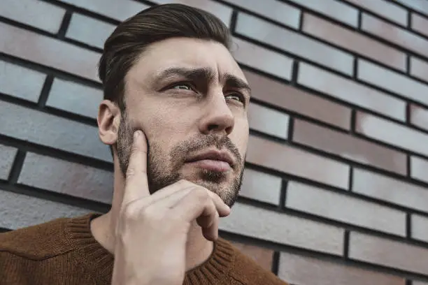 Photo of Young hipster guy wearing have some ideas on brick wall background.