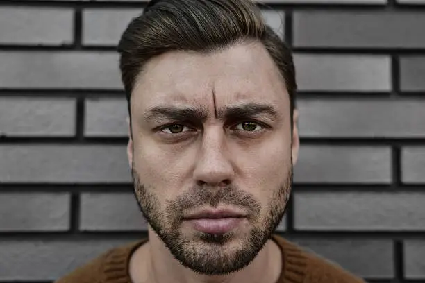 Photo of Portrait of serious manly stunning man in sweater looking at camera standing on street.