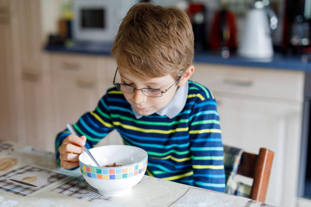 사랑 스러운 행복 한 작은 금발 아이 소년 안경 만든 시리얼 아침 식사 또는 점심 식사. 건강 한 어린이 위한 식 생활. 보육, 학교 식당에서 또는 가정에서 - eating cereal student human mouth 뉴스 사진 이미지