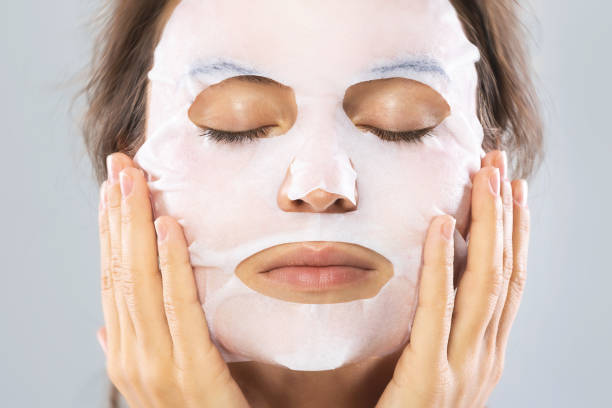istock Woman with a sheet moisturizing mask on her face isolated on gray background 1083384076