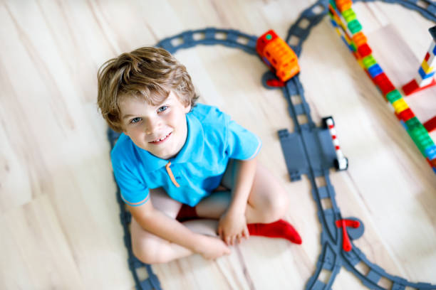 istock Adorable little blond kid boy playing with colorful plastic blocks and creating train station. Child having fun with building railway toys at home.. 1083385480