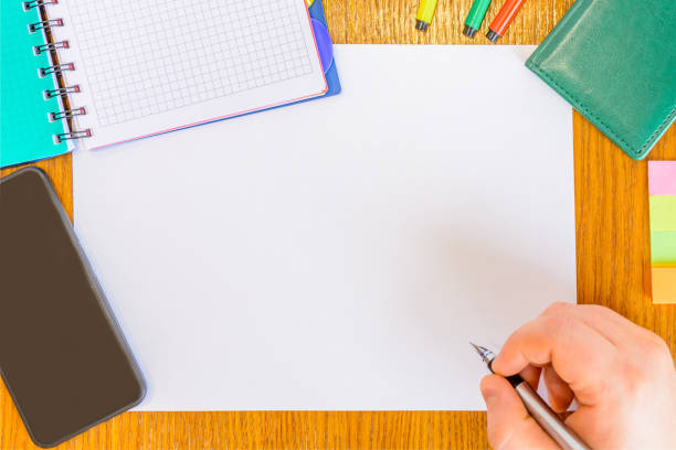 istock Man's hand with pen writing on the white paper (draft). Man working on the desk using phone, notepad, pen, felt-tip pen, diary. Work organization. 1083385788
