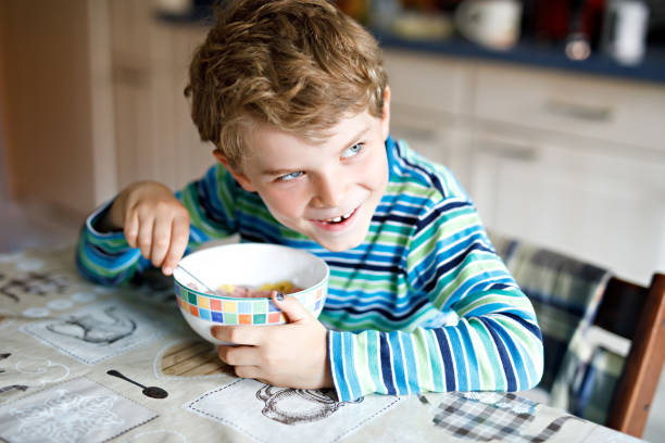 사랑 스러운 작은 금발 학교 아이 소년 먹는 우유와 딸기 시리얼 아침 이나 점심에 대 한. 건강 한 아이 들, schoolkids 위한 식 생활. 학교 식당에서 또는 가정에서 - eating cereal student human mouth 뉴스 사진 이미지