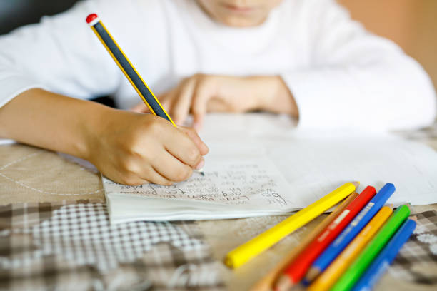 Child doing homework and writing story essay. Elementary or primary school class. Closeup of hands and colorful pencils stock photo