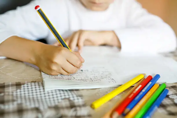 Photo of Child doing homework and writing story essay. Elementary or primary school class. Closeup of hands and colorful pencils