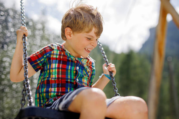 istock Funny kid boy having fun with chain swing on outdoor playground while being wet splashed with water. child swinging on summer day. Active leisure with kids. Happy crying boy with rain drops on face. 1083388524
