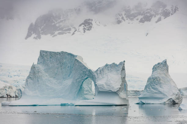 Antarctica Iceberg Natural Arch Neumeyer Channel Antarctica Neumeyer Channel Iceberg with Natural Ice Arch in front of Antartica Peninsula Glaciers drifting on the Antarctic Ocean. Neumeyer Channel, Antarctic Ocean, Antarctica. iceberg dramatic sky wintry landscape mountain stock pictures, royalty-free photos & images