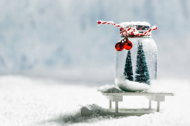 Christmas ornaments on snow Christmas ornaments of glass jar with striped ribbon , bells and fir trees inside on snow background snow jar stock pictures, royalty-free photos & images