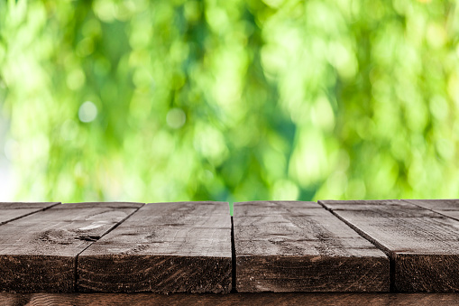 Empty rustic wooden table with defocused lush foliage at background. Ideal for product display on top of the table. Predominant color are green and brown. DSRL studio photo taken with Canon EOS 5D Mk II and Canon EF 100mm f/2.8L Macro IS USM.