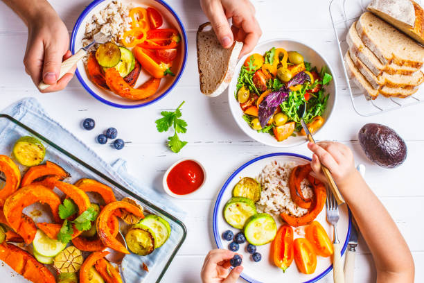family eating a healthy vegetarian food. vegan lunch table top view, plant based diet. baked vegetables, fresh salad, berries, bread on a white background. - healthy eating food rice high angle view imagens e fotografias de stock