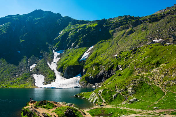 Lake Balea of Fagaras mountains Lake Balea of Fagaras mountains. last pieces of snow on the grassy hills. beauty of Romania balea lake romania stock pictures, royalty-free photos & images