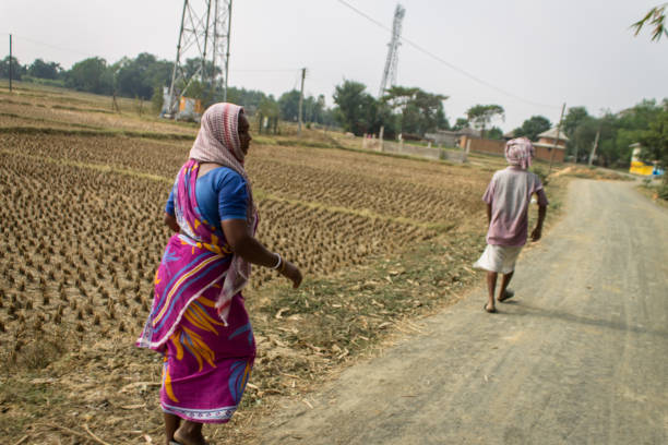 Bolpur, WB, India - November 30, 2018 : A man and woman in traditional clothing walking on a dirt country road in rural India alongside paddy fields.