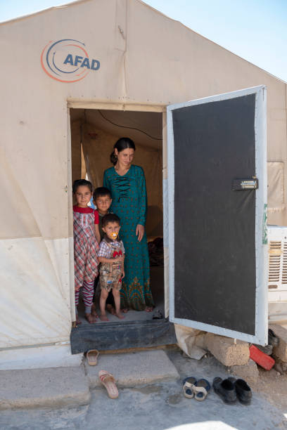 Yazidi mother and children in IDP camp Sharya, Iraq - May 28, 2017: A young Yazidi woman stands with her three children inside a tent in Sharya IDP camp in northern Iraq, their home for the past several years. They and their neighbors fled the 2014 ISIS advance in which many Yazidis were killed and others, especially women and children, captured and trafficked by ISIS. islamic state stock pictures, royalty-free photos & images