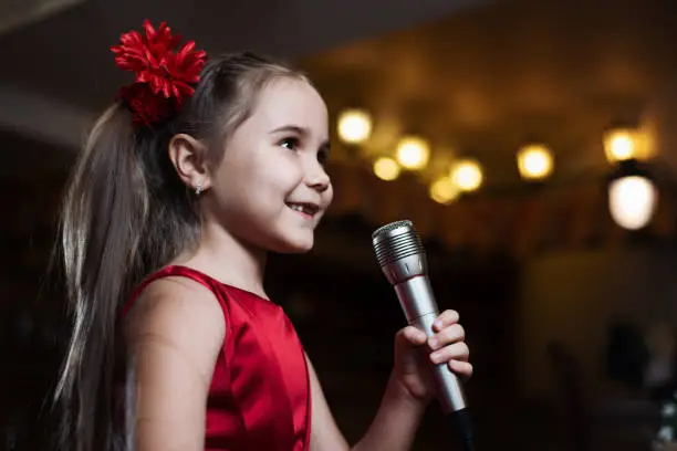 Photo of The girl with the microphone. A small child sings karaoke closeup