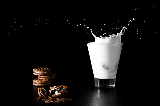 Splash in glass of milk and chocolate cookies on black background.